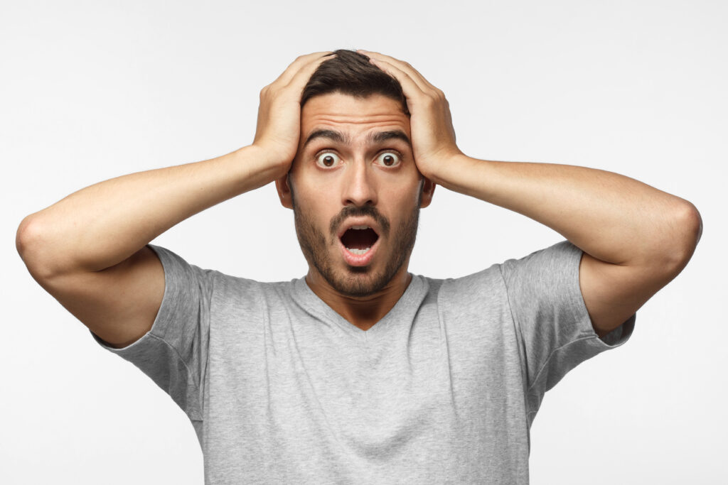 Shock content. Surprised young male in gray t-shirt shouting, holding his head with both hands